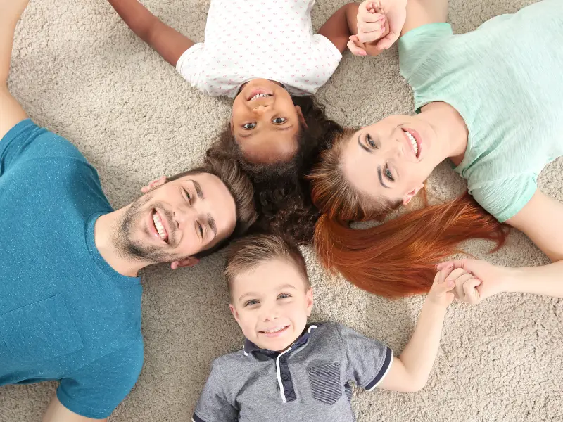 A smiling family lies head to head on a beige carpet, reflecting the clean, healthy comfort promoted by ZeroChem Las Vegas residential services.